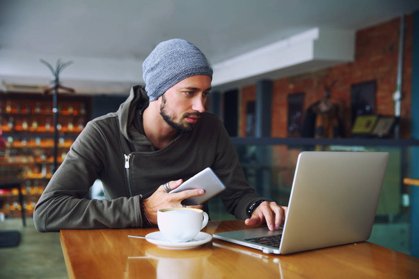Młody przystojny mężczyzna z brodą jest za pomocą komputera w kawiarni - Zdjęcie, obraz