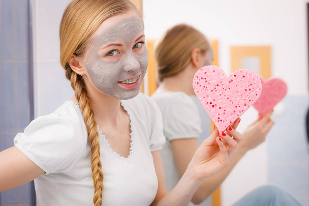 Woman having grey face mask holding heart sponge - Foto, afbeelding