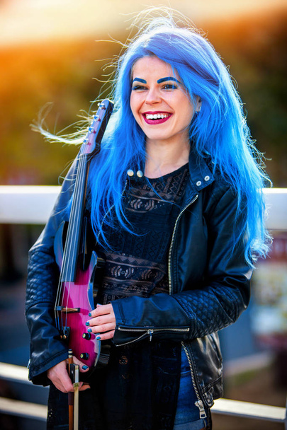 Blue hair woman buskers with violin outdoor in sun shine
. - Фото, изображение