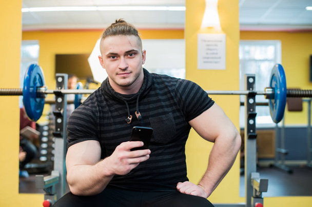 Jovem homem bonito usando telefone enquanto faz exercício no ginásio
. - Foto, Imagem