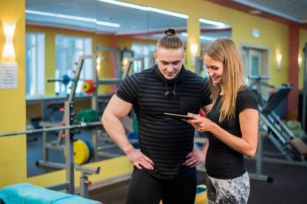aantrekkelijke jonge paar passen bij een sportschool op zoek op een tablet-pc als zij hun vooruitgang en fitness controleren - Foto, afbeelding