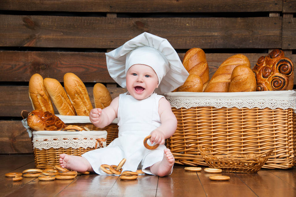 Child cooks a croissant in the background of baskets with rolls and bread. - Photo, Image