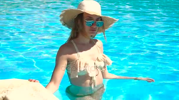 young girl in a bathing suit and hat glasses stands in the pool and turns her head to the side in slow motion - Záběry, video