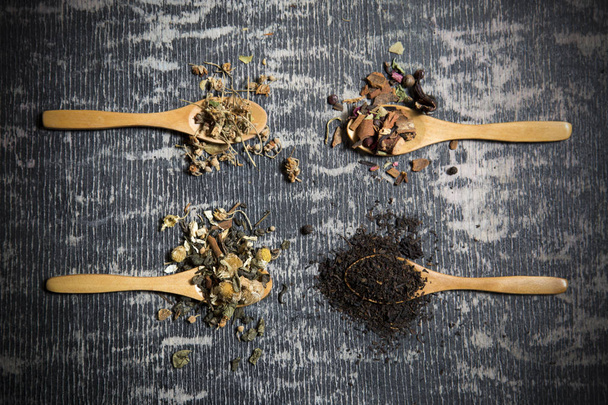 Food background with different black and green dry tea, rose buds cup of hot tea and iron teapot over dark wooden background. Tea drinking concept. Top view. Square image - Photo, Image