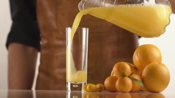 Man in leather apron pours juice on table with oranges and mandarines - Кадры, видео