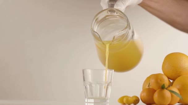 Orange juice pours in a glass on table with oranges and mandarines - Filmati, video