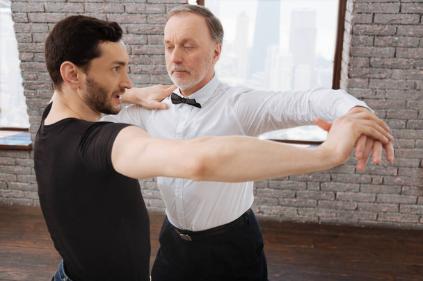 Helpful dance teacher tangoing with aged man at the ballroom - Foto, afbeelding