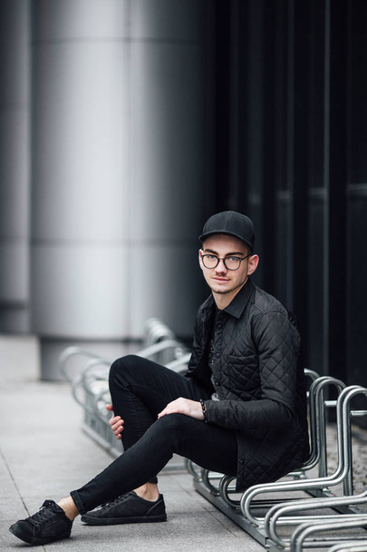 Fashionable man sitting near the wall with glasses on hands - Valokuva, kuva