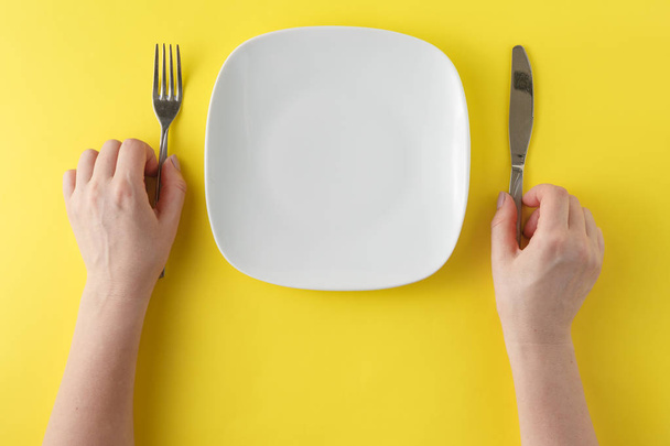 woman two hands hold a spoon and fork and white dish on yellow b - Photo, Image