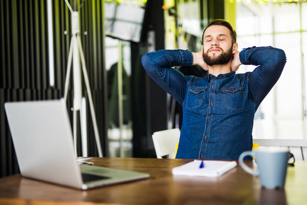 Young bearded man relaxing at his desk in office - 写真・画像
