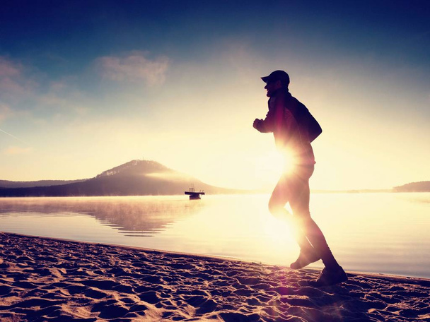Sylwetka sport active człowiek działa na plaży nad jeziorem o wschodzie słońca. Zdrowy styl życia.  - Zdjęcie, obraz