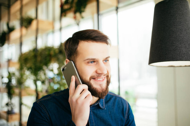 Komea liikemies rento kuluminen puhuu matkapuhelimeen, eleiden seistessään toimistossa
 - Valokuva, kuva