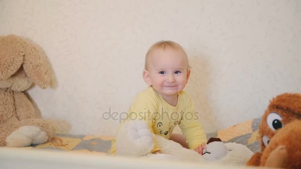Smiling cute baby looking to camera and playing with teddy bear - Imágenes, Vídeo