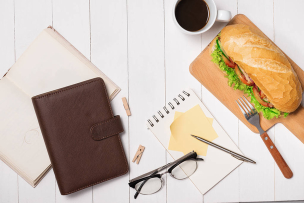 Snack at break time. Healthy business lunch in office, top view of Vietnamese sandwich, or Ban Mi on white wooden desk with coffee, mobile phone and notepad with pen flat lay. - Фото, изображение