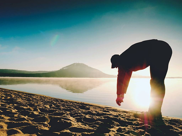 Man exercising on beach.  Silhouette of active man exercising  and stretching at lake - Foto, Imagen