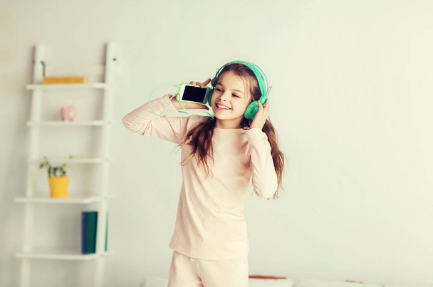 girl jumping on bed with smartphone and headphones - Foto, Imagem