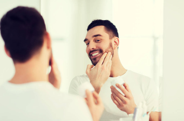 happy young man applying cream to face at bathroom - Photo, image