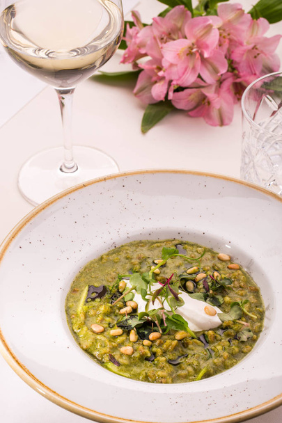 Table layout. Orzotto with goat cheese and spinach. Giving on a round plate with a glass of white wine and fresh flowers - Foto, Bild