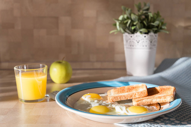 Fried eggs on decorative plate with toasted bread, green apple and orange juice - Zdjęcie, obraz