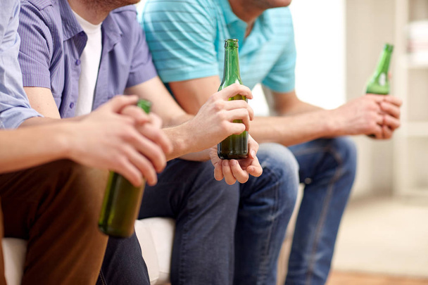 men with beer bottles sitting on sofa at home - Foto, Bild
