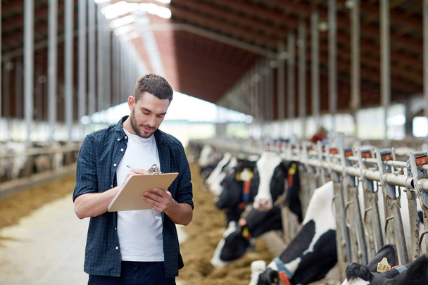 farmer with clipboard and cows in cowshed on farm - Foto, Bild
