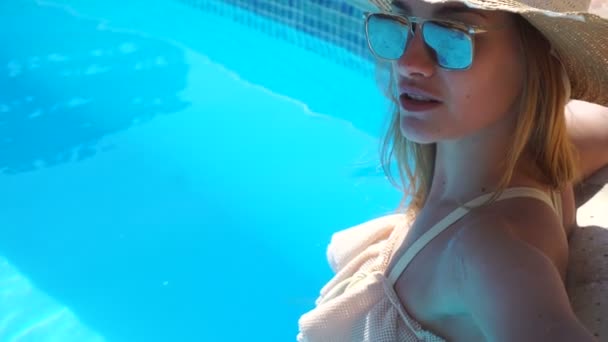 a young girl wearing a hat and glasses through which visible water pool looks into a camera - Záběry, video