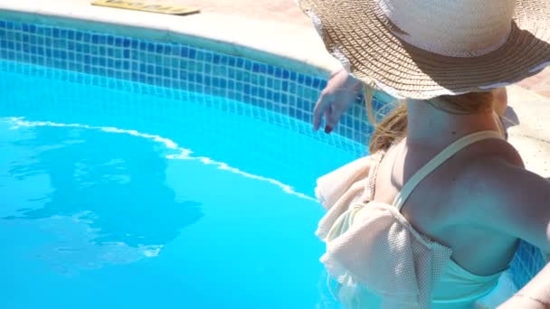 a young girl in a bathing suit and hat stands in pool unscrewing the head back - Záběry, video