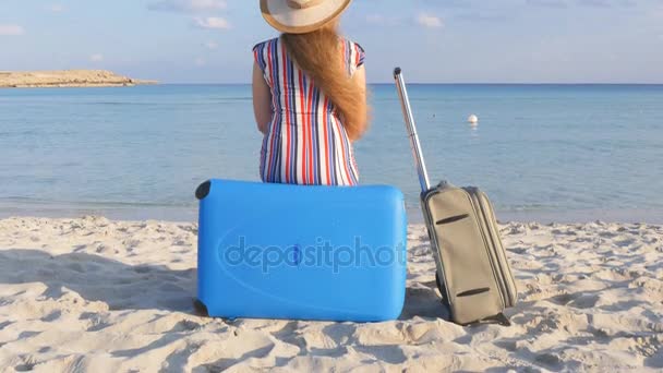 Młoda kobieta z walizką siedzi na plaży - Materiał filmowy, wideo