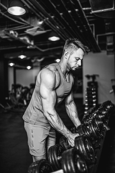 Handsome muscular man is working out and posing with dumbbells at a gym - Foto, imagen