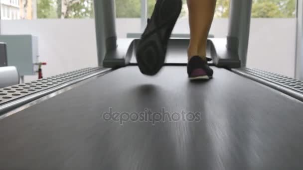 Női lábak fut a futópadon a tornateremben. Fiatal nő gyakorlása során kardió edzés. Lábak a lányok képzés fedett sport Club sport cipő. Közelről - Felvétel, videó