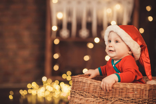 Μικρό αγοράκι στο Santa καπέλο που κάθεται σε ένα καλάθι λυγαριά - Φωτογραφία, εικόνα