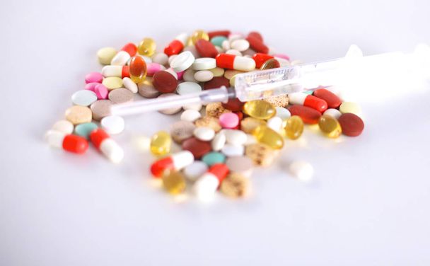 Tabletten und eine Spritze liegen auf einem weißen Tisch - Foto, Bild