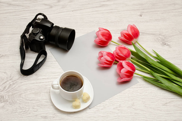 Różowe tulipany na pusty arkusz papieru, kubek herbaty i aparat, jasnym tle drewnianych. - Zdjęcie, obraz