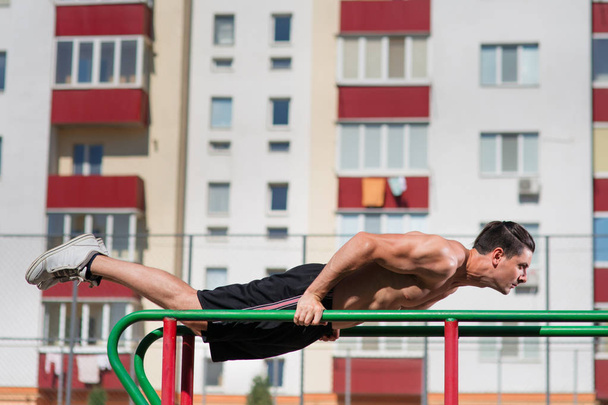 Fit man workout out arms on dips horizontal bars training triceps and biceps doing push ups outdoors. - Fotoğraf, Görsel