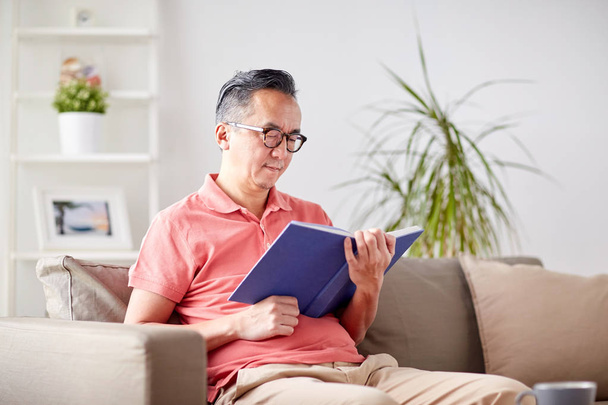man sitting on sofa and reading book at home - Photo, Image