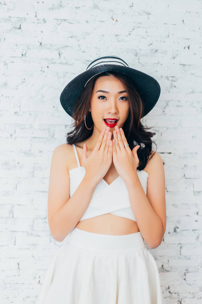 Young woman giving surprise look with fashionable summer hat over white wall background - Foto, Imagen