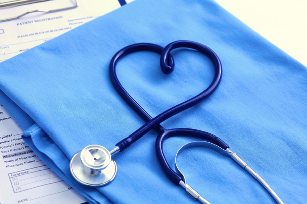 Stetoskop lekarskie skręcone w kształcie serca, leżącego na liście historię choroby pacjenta i lekarza niebieski jednolite zbliżenie. Pomocy medycznej lub koncepcja ubezpieczeń. Kardiologia, zdrowia, ochrony i zapobiegania - Zdjęcie, obraz
