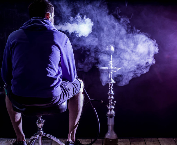 ein Mann raucht eine Wasserpfeife auf schwarzem Hintergrund, schöne Beleuchtung - Foto, Bild
