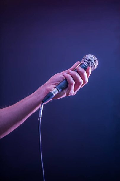 mão com microfone em um fundo preto, o conceito de música, iluminação bonita no palco
 - Foto, Imagem