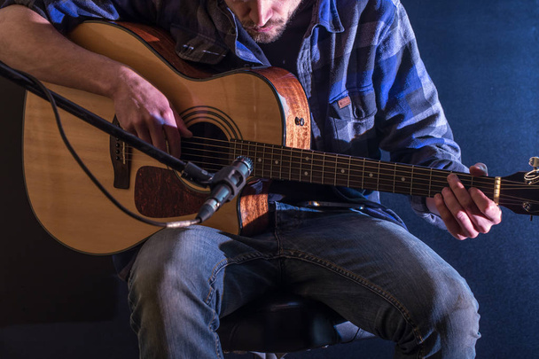 ο άνθρωπος που παίζουν ακουστική κιθάρα πάνω σε μαύρο φόντο, η έννοια της μουσικής, όμορφο φωτισμό στη σκηνή - Φωτογραφία, εικόνα