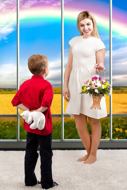 Young beautiful mother with her son and a bouquet of flowers. The child gives the mother a small Teddy bear, surprise.Spring concept of family vacation. Women's day - Foto, Imagen