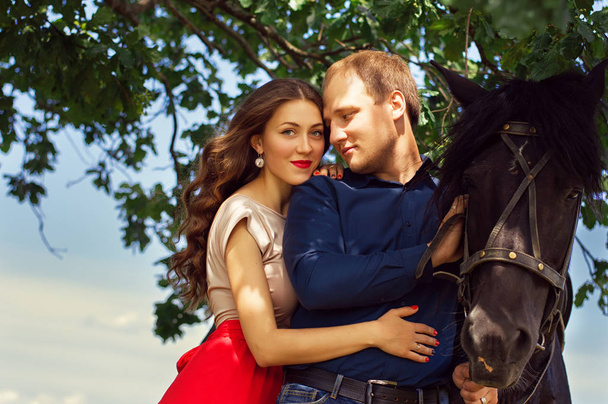 幸せなカップルの肖像画は、黒い馬の近くに立ってスマート カジュアルな服に身を包んだ。家族の概念。デート。愛とロマンチックな - 写真・画像