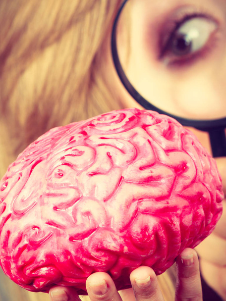 Woman holding magnifying glass investigating brain - Foto, Imagen