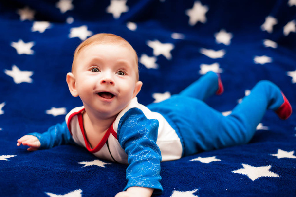 Niño de 6 meses y sonriendo en casa sobre una manta azul del cielo estrellado
 - Foto, Imagen