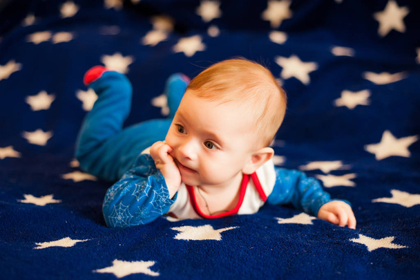 Niño de 6 meses y sonriendo en casa sobre una manta azul del cielo estrellado
 - Foto, Imagen