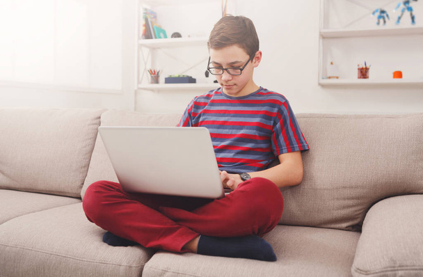 Teini-ikäinen poika käyttää kannettavaa tietokonetta sohvalla kotona
 - Valokuva, kuva
