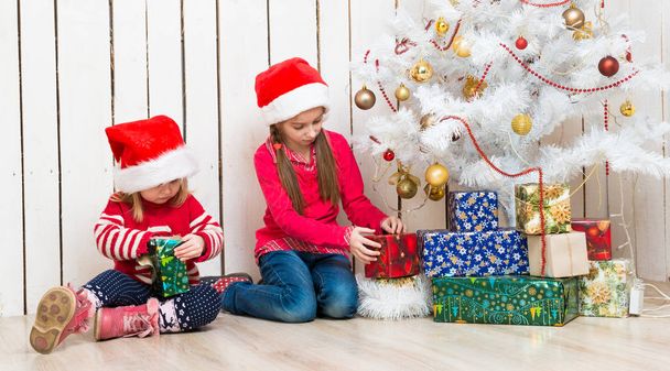 две маленькие девочки открывают рождественские подарки сидя на полу - Фото, изображение