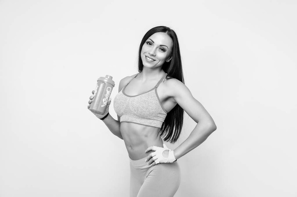 Muscular woman in leggings, top and gloves having a rest, standing and holding shaker - Фото, зображення