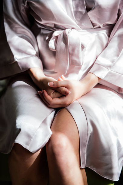 A girl in a silk robe sits on a chair and crosses her hands on h - Photo, image