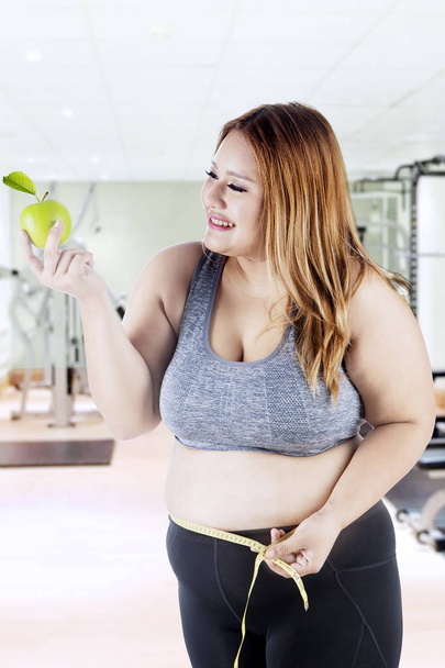 Fat woman holds apple at gym - Photo, image